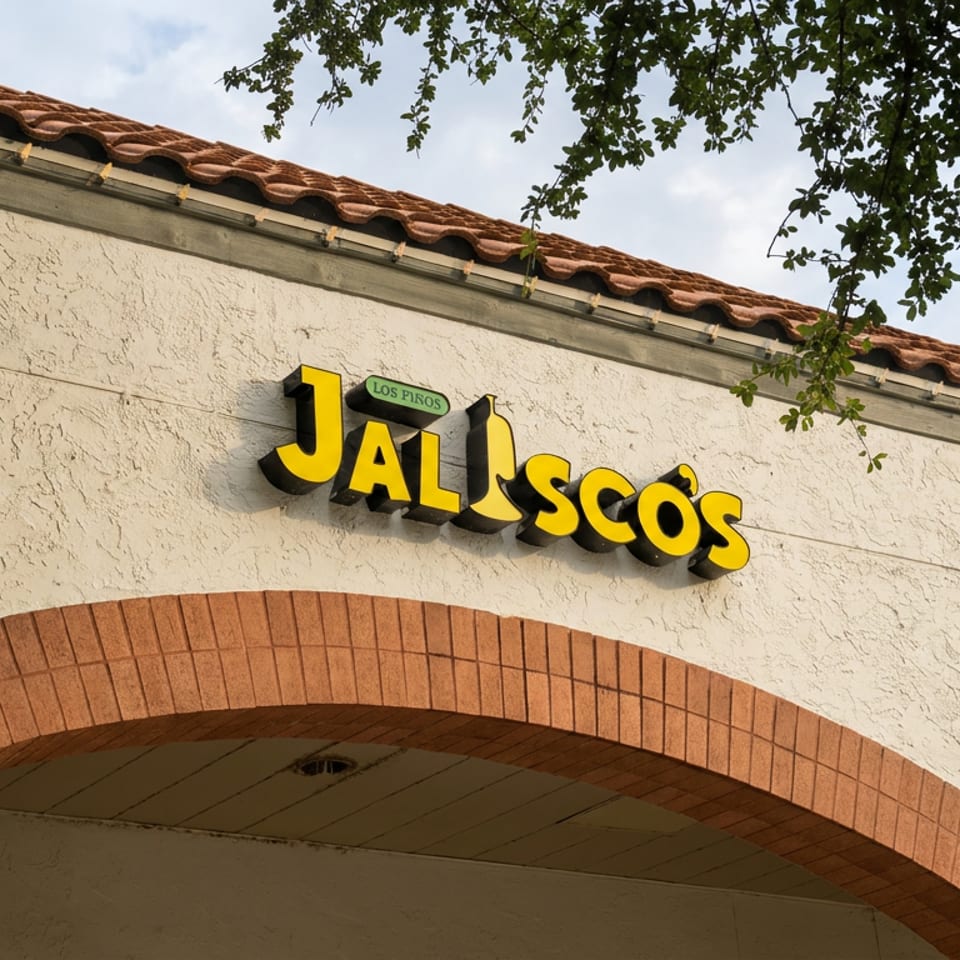 Los Perros Jalisco restaurant sign above a brick archway on a stucco building with Spanish-style tile roofing.