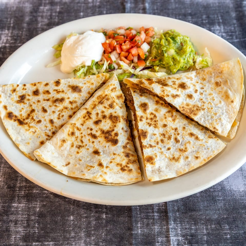 Grilled quesadilla wedges served with shredded lettuce, pico de gallo, guacamole, and sour cream on a white platter.
