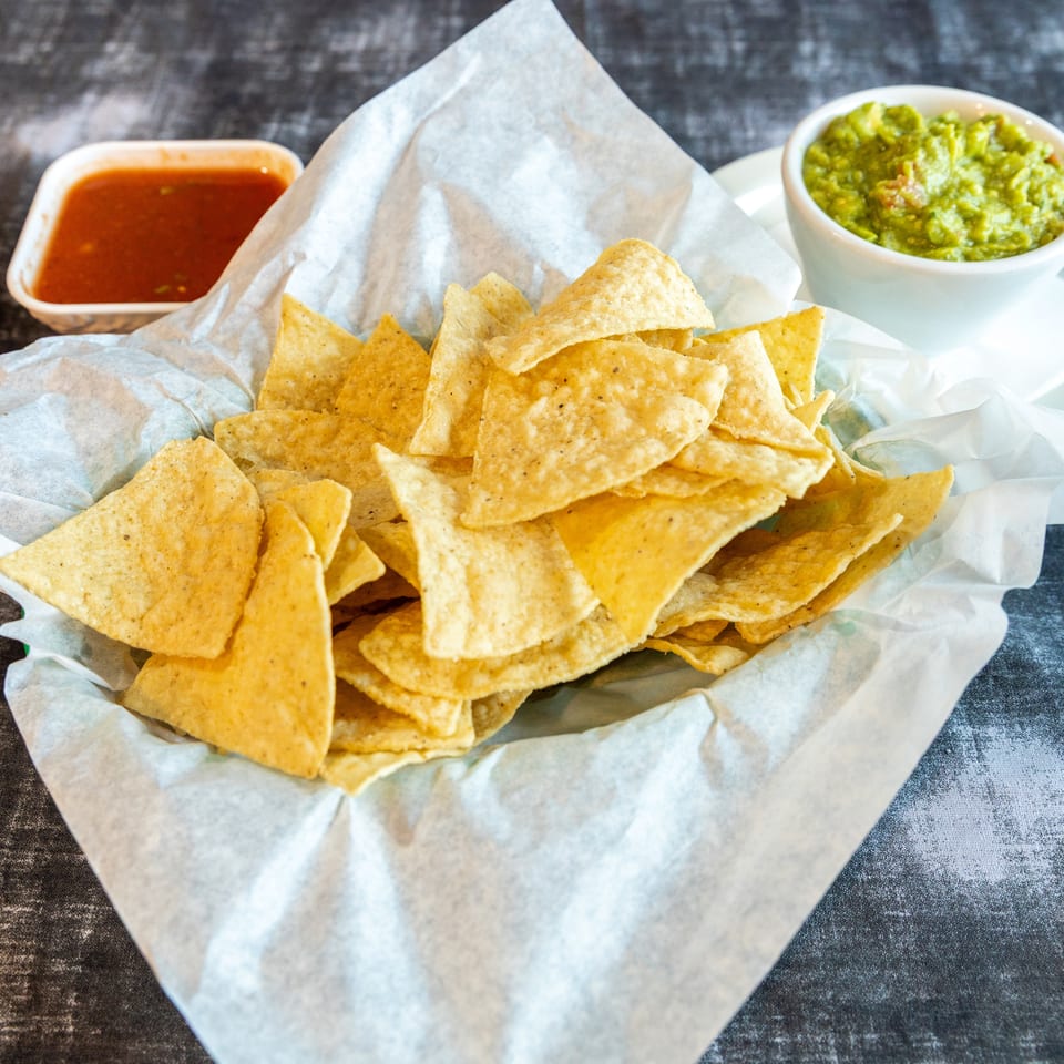 Basket of crispy tortilla chips served with red salsa and fresh guacamole on a restaurant table.