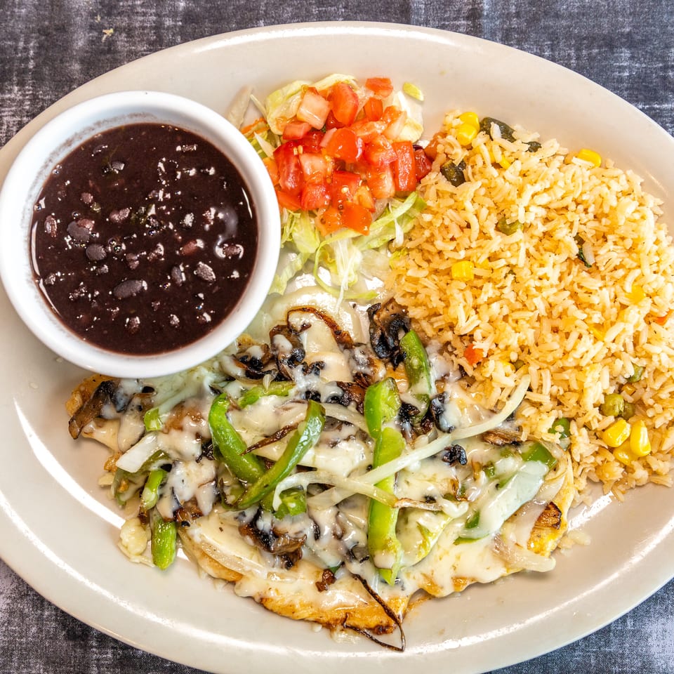 Plate of cheesy grilled chicken topped with mushrooms, peppers, and onions, served with vegetable rice, black beans, and tomato salad.