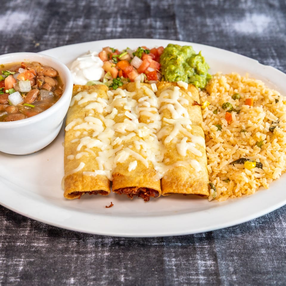 Mexican platter with cheese-drizzled rolled enchiladas, Mexican rice, beans, guacamole, pico de gallo, and sour cream.