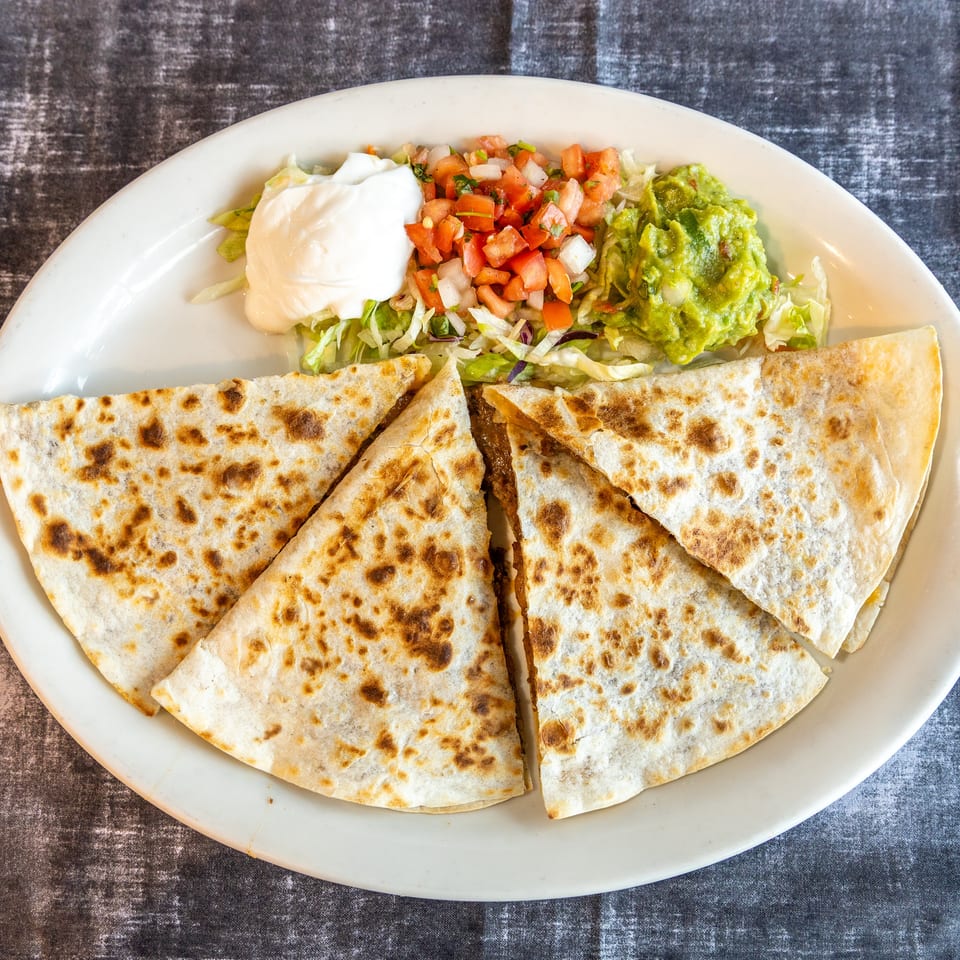 Grilled quesadilla wedges served with shredded lettuce, sour cream, pico de gallo, and guacamole on a white plate.