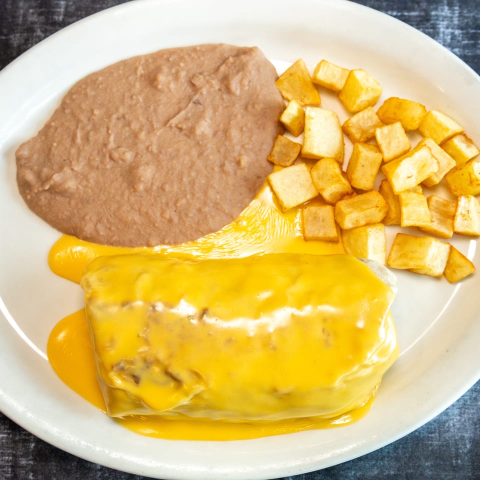 Plate of cheesy enchiladas with refried beans and golden diced potatoes.