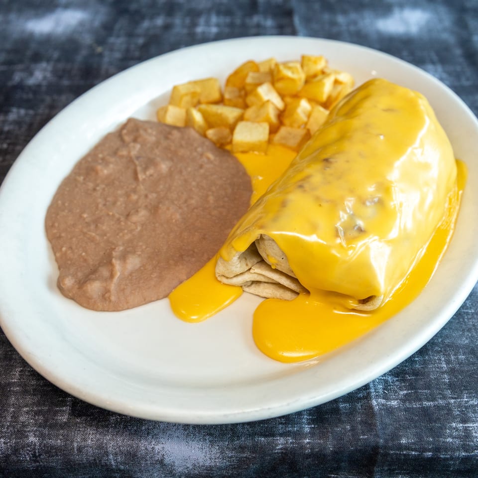 Plate of enchiladas covered in melted cheese, served with refried beans and diced potatoes.
