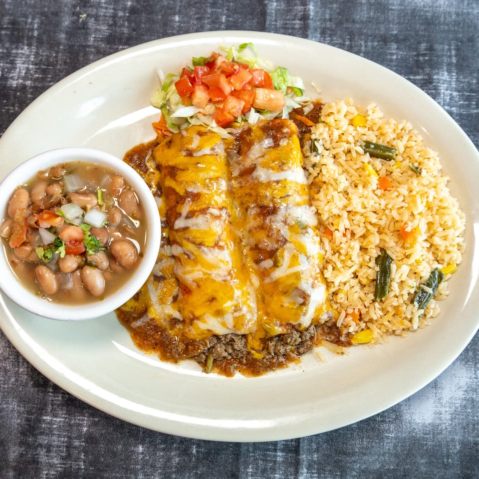 Cheesy enchiladas topped with sauce, served with Mexican rice, pinto beans, and a fresh lettuce-tomato salad.