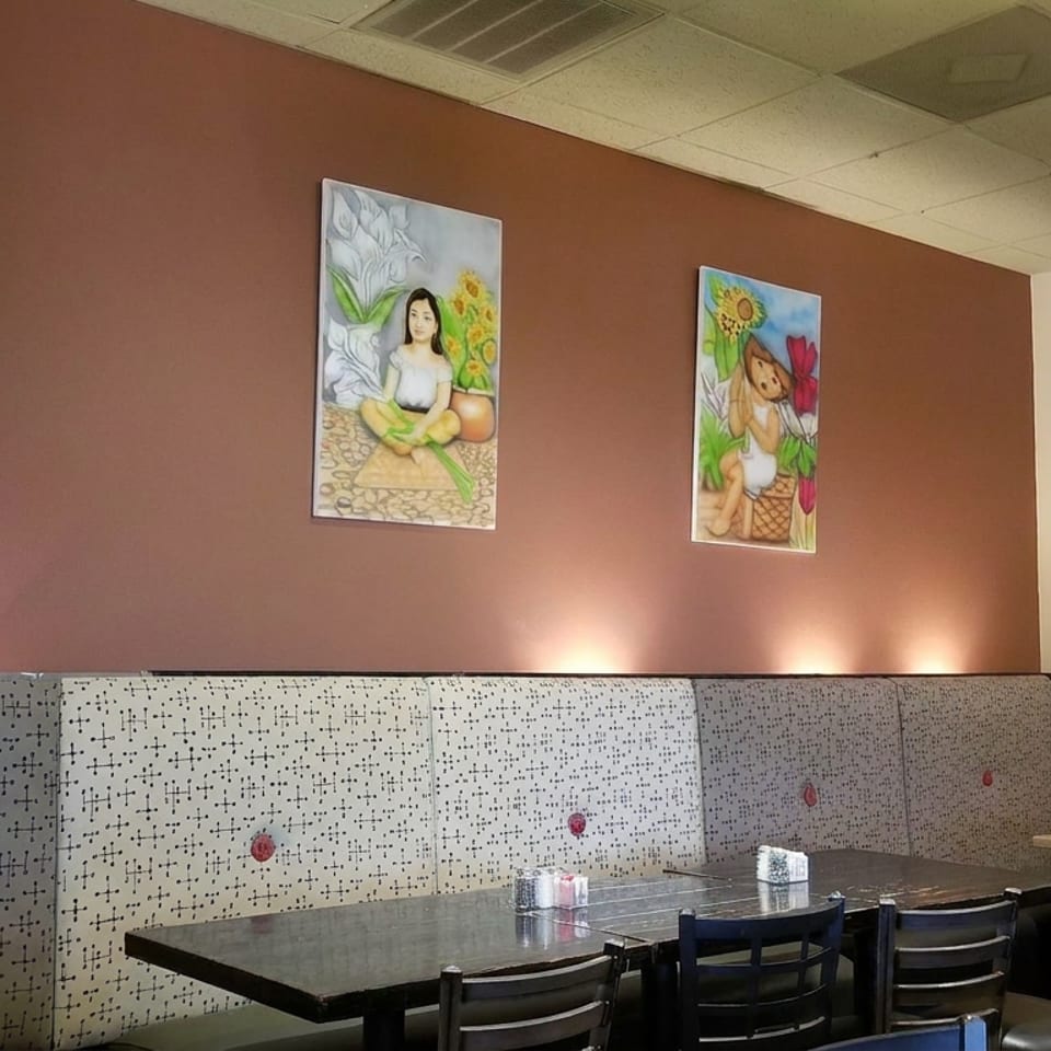 Restaurant dining area with patterned booth seating, tables, and colorful paintings depicting people and children on the walls.