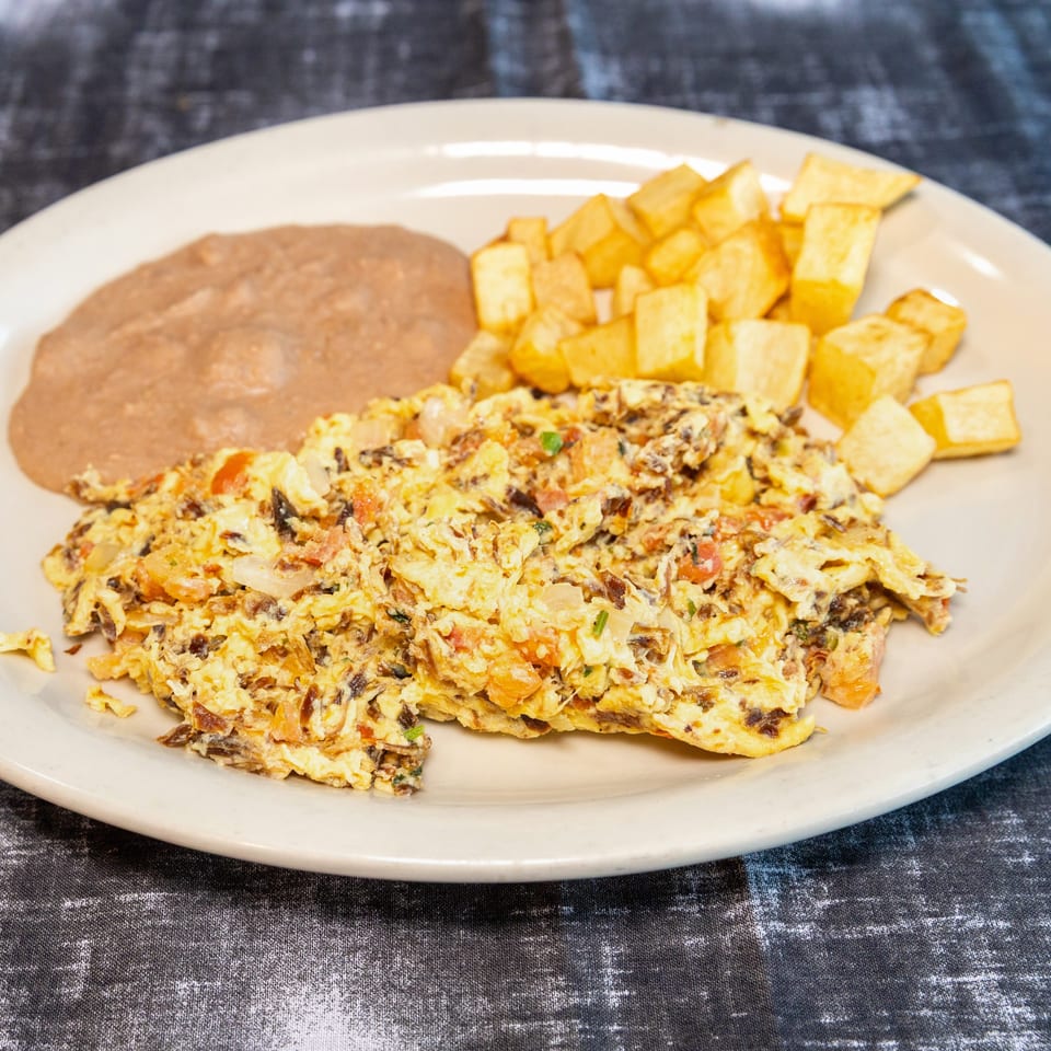 Scrambled eggs with vegetables, refried beans, and golden fried plantains served on a white plate.