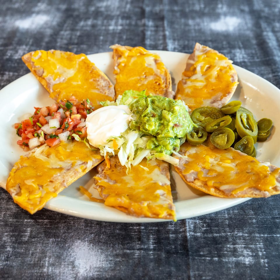 Cheesy Mexican nachos topped with guacamole, sour cream, pico de gallo, lettuce, and sliced jalapeños on a white plate.