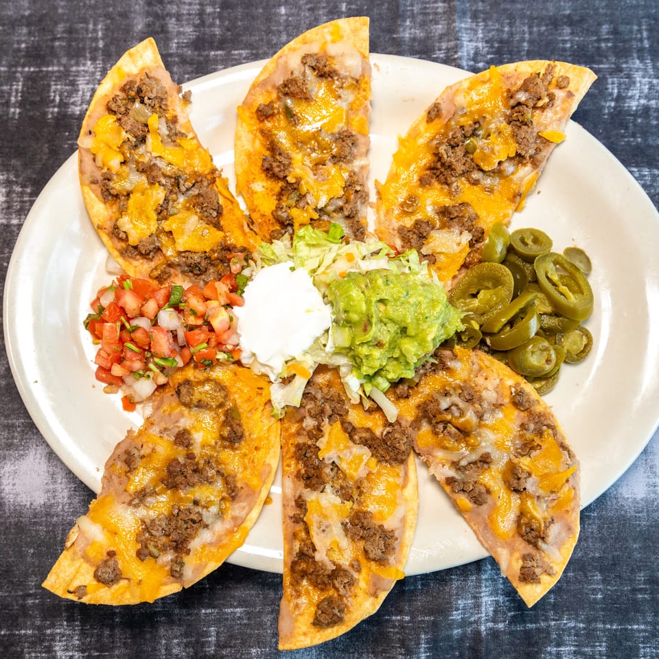 Plate of cheesy ground beef nachos topped with lettuce, guacamole, sour cream, pico de gallo, and sliced jalapeños.