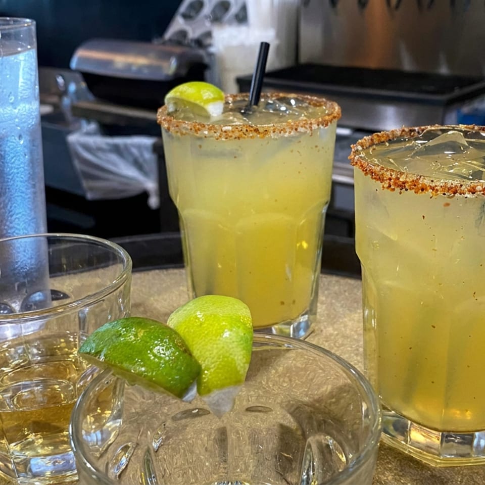 Two salted-rim lime cocktails, a whiskey glass, and a water glass arranged on a restaurant bar tray.