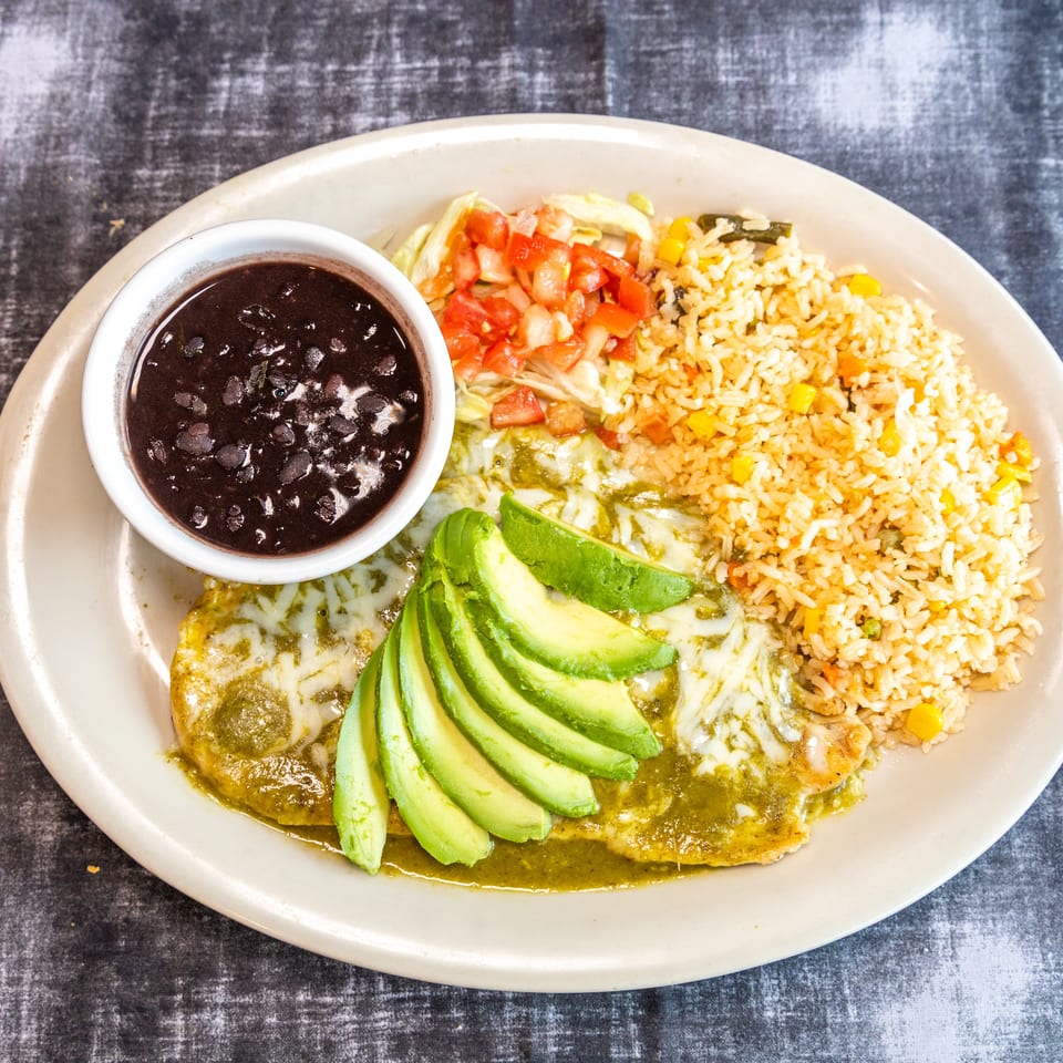 Mexican-style platter with avocado-topped enchiladas, seasoned rice, salad, and a bowl of black beans.